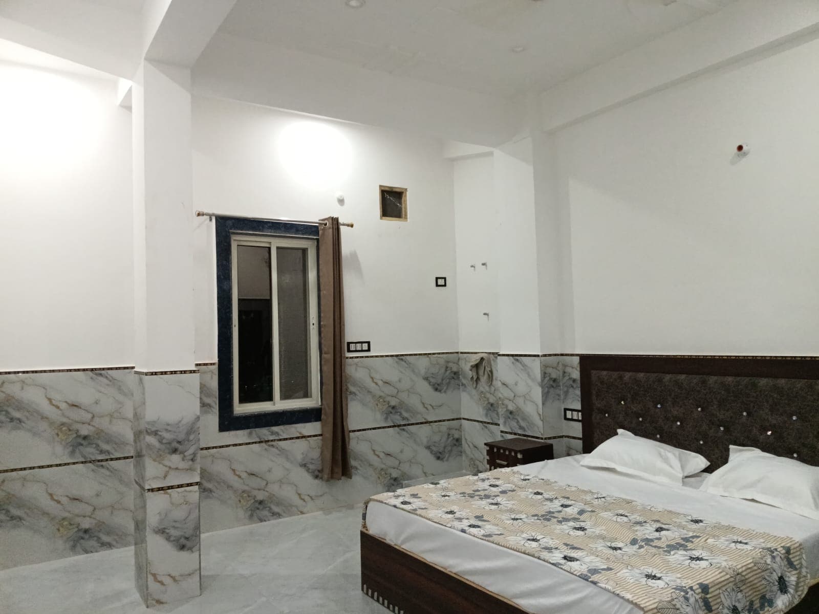 Deluxe AC room with a double bed, marble-finish tiled walls and a window