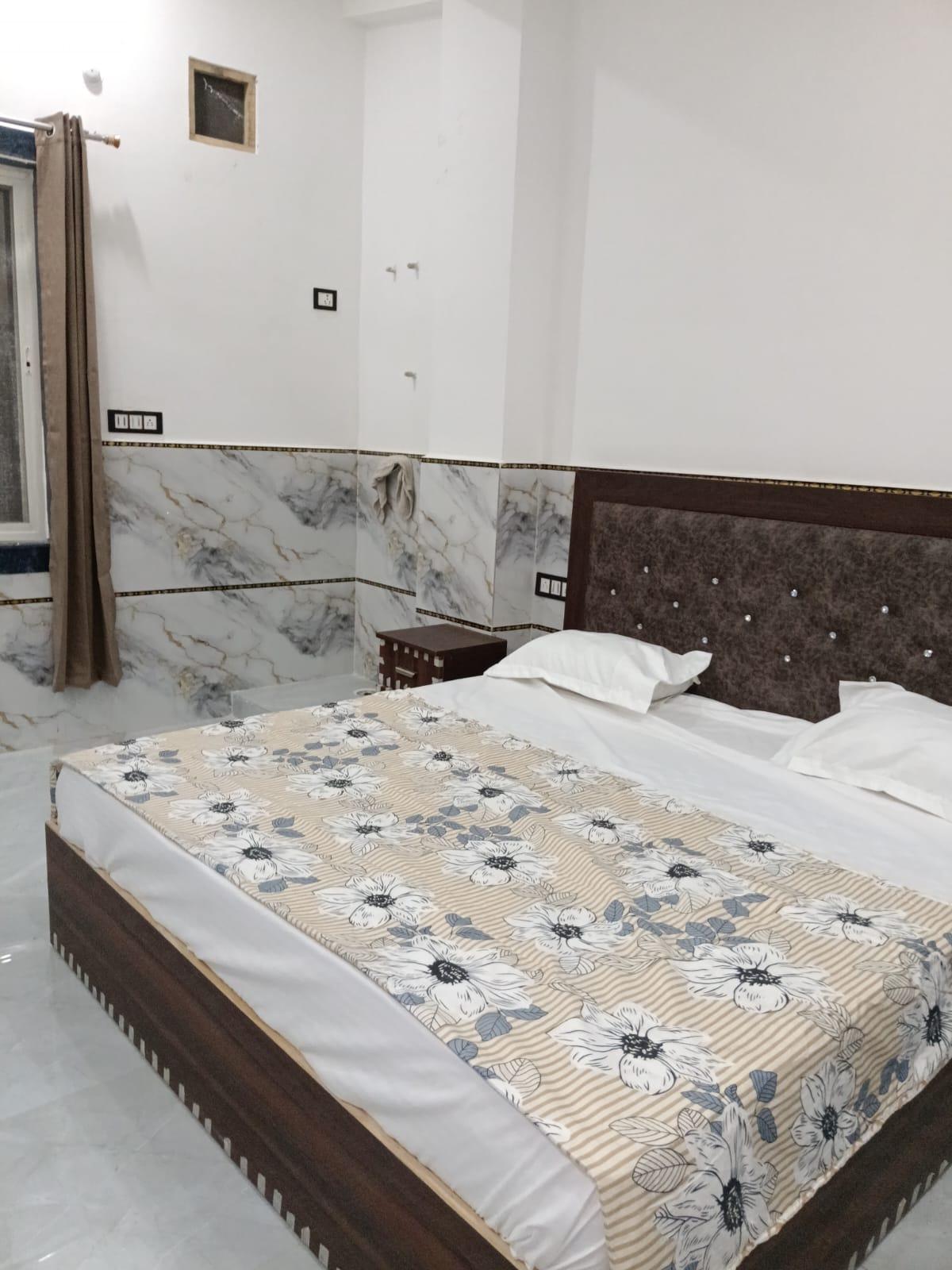 Double bed beside a curtained window with marble-finish tiled walls